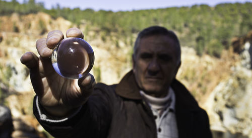 Close-up portrait of man holding sphere against rock formations