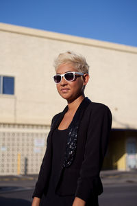 Portrait of young woman wearing sunglasses standing against clear sky