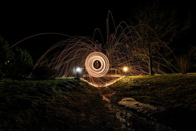 Man spinning wire wool on footbridge over river at night