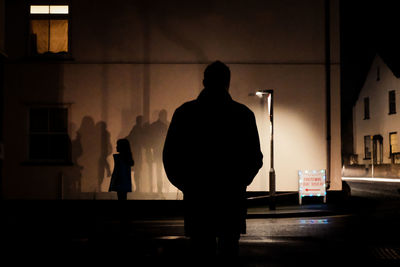 Rear and side  view of silhouette man and girl standing by building 