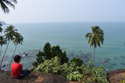Rear view of woman sitting by sea against sky