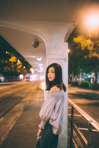 Portrait of smiling young woman standing against illuminated lights