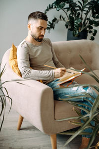 Man writing in book while sitting on sofa