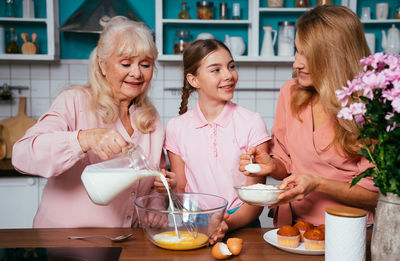 Cheerful daughter with parents preparing food at kitchen