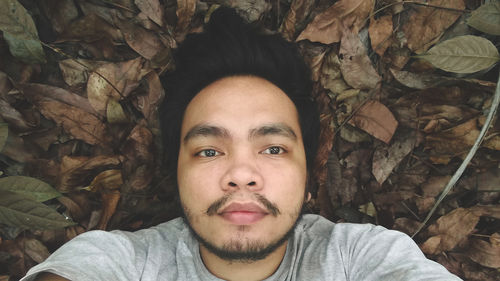 Portrait of young man lying on autumn leaves