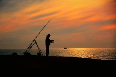 Silhouette man fishing in sea against sunset sky