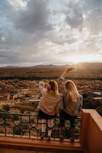 Rear view of women standing on landscape against cloudy sky