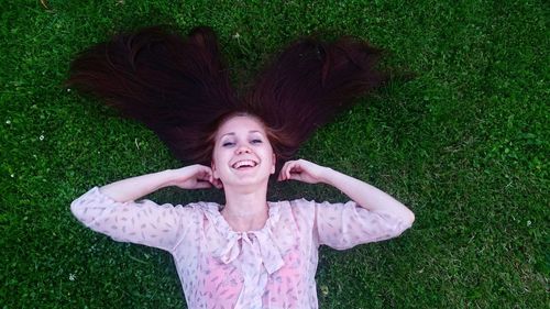 Directly above portrait of cheerful woman lying on grassy field