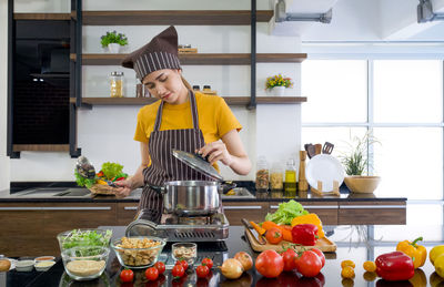 Young housewife dressed in an apron and a hair cap, preparing the meat stew in a modern kitchen.