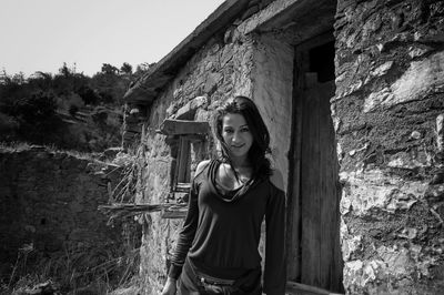 Portrait of young woman standing by abandoned house