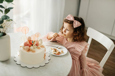 Cute little girl eats a birthday cake with a spoon on her birthday