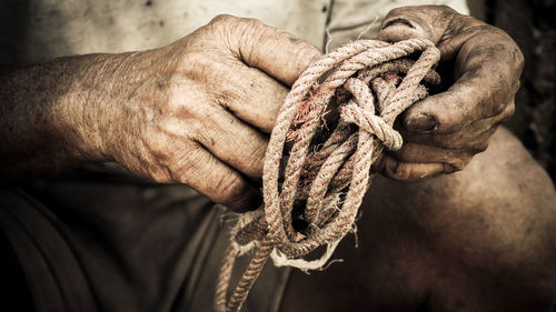 Midsection of old man tying rope