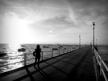 Full length of woman standing on bridge over boats moored at sea against sky