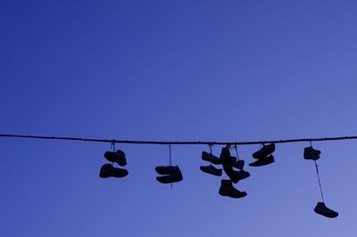 Low angle view of shoes hanging on cable against clear sky