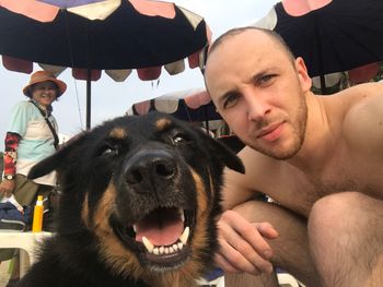 Low angle portrait of shirtless man with dog at beach