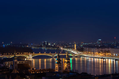 Illuminated bridge over river in city at night