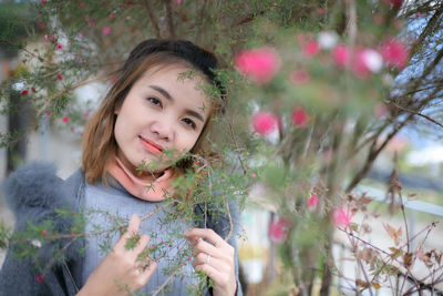 Portrait of woman holding flowering plants against trees