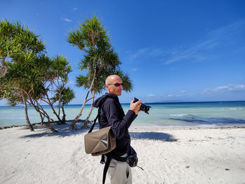 Portrait of young man standing at beach against sky