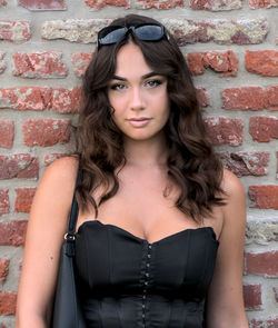 Close portrait of a brunette woman, with brown eyes, long hair and sunglasses. red bricks background