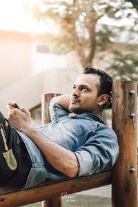 Young man using mobile phone while sitting on wood