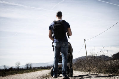 Rear view of man with baby carriage standing on field against sky during sunny day