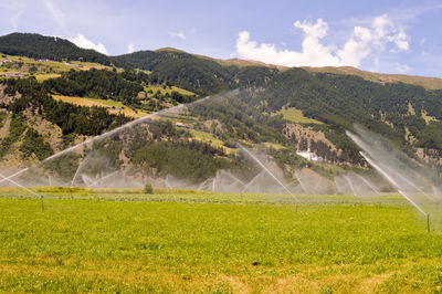 Sprinkler on grassy field against mountain