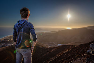 Rear view of man standing on mountain at sunset