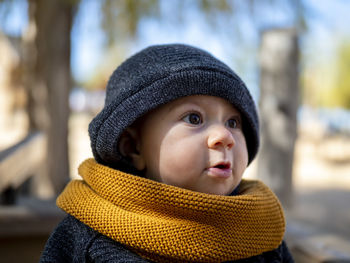 Close-up of cute girl wearing sweater and knit hat sitting at park