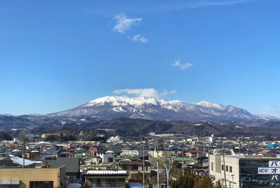 Aerial view of townscape and mountains against blue sky