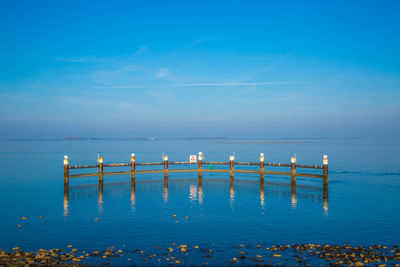 Metal railing with reflection in sea against sky