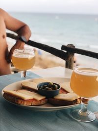 Midsection of person with drink on table by sea against sky