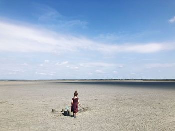 Rear view of girl walking by sandcastle at beach against sky