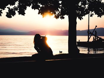 Silhouette man sitting on beach against sky during sunset