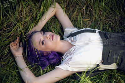 Portrait of a teenage girl with purple hair and an earring in her nose lying in the grass in nature