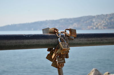 Close-up of padlocks on railing by river against sky