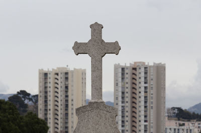 Low angle view of cross amidst buildings against sky