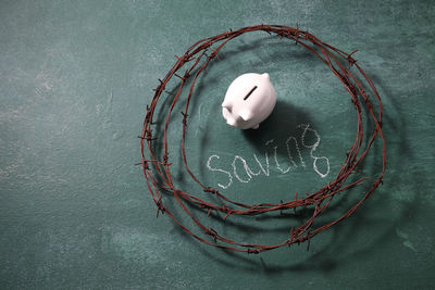 High angle view of rusty barbed wire with piggy bank and saving text on blackboard