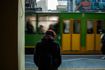 Rear view of man standing at railroad station platform in city