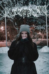 Portrait of young woman standing by tree during winter