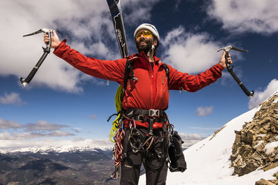 Man looking away with arms outstretched standing against sky during winter