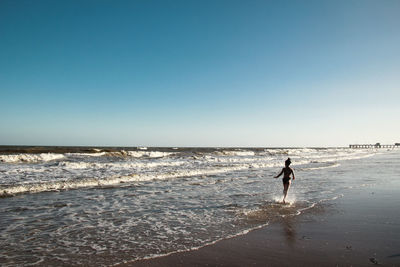 Rear view of girl running at shore against clear sky