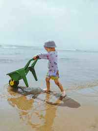 Boy climbing on beach against sky