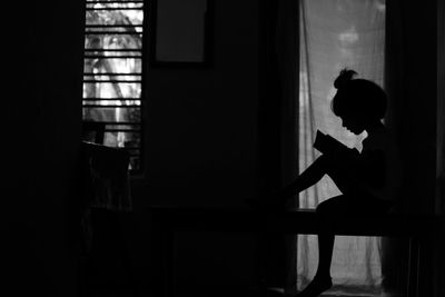 Side view of silhouette woman standing against window at home