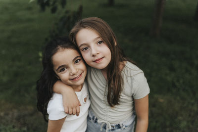 Portrait of smiling sisters standing with arm around at park