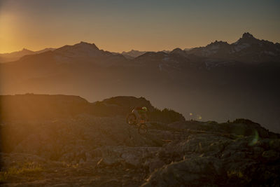 Full length of man cycling on rock against mountain range