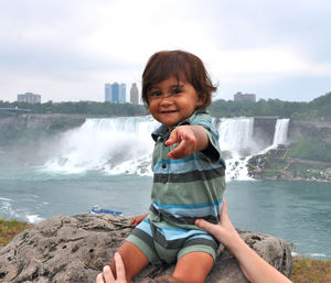 Portrait of cute boy sitting on rock against waterfall