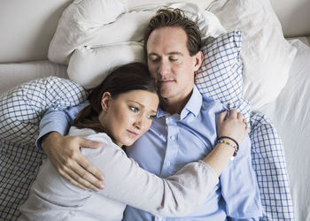 High angle view of sad woman embracing man while lying in bed