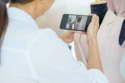 Rear view of fashion designer photographing dress on mannequin in office