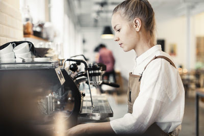 Side view of young female barista using espresso maker at cafe