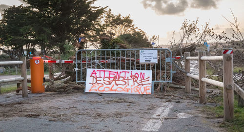 Sign board by trees against sky